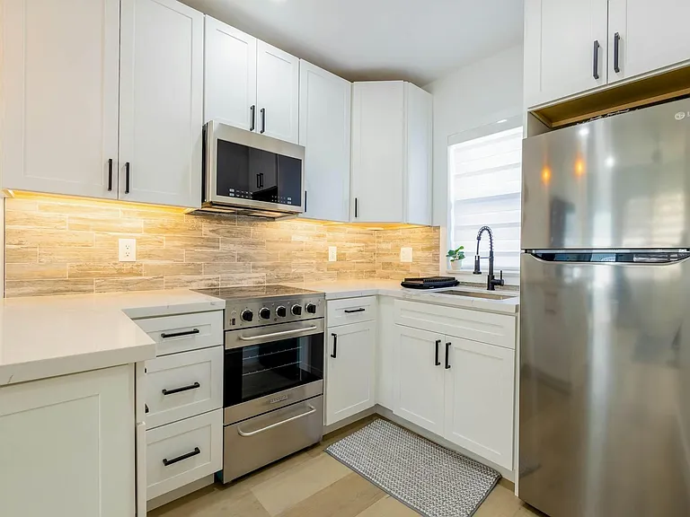 Updated kitchen with shaker cabinetry, quartz-style counters, tile backsplash, and stainless appliances plus a windowed sink.
