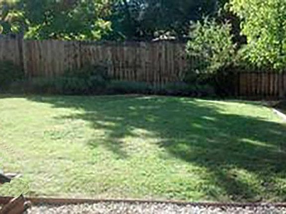Large lawn in the backyard with a graveled area just inside the fence for a boat or small RV storage.