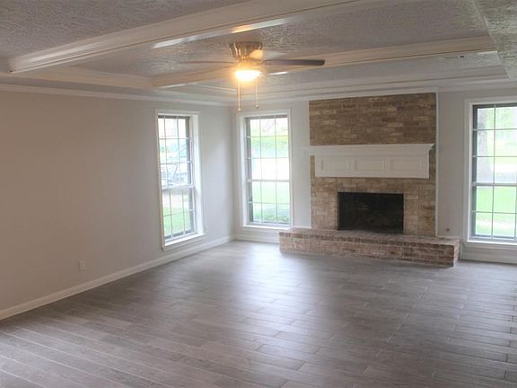 Family den. Ceiling Fan. Storm windows covering windows for better insulation. Tile wood floor. Gray neutral walls. Decorative wood beams across the ceiling. Gas Fire place.