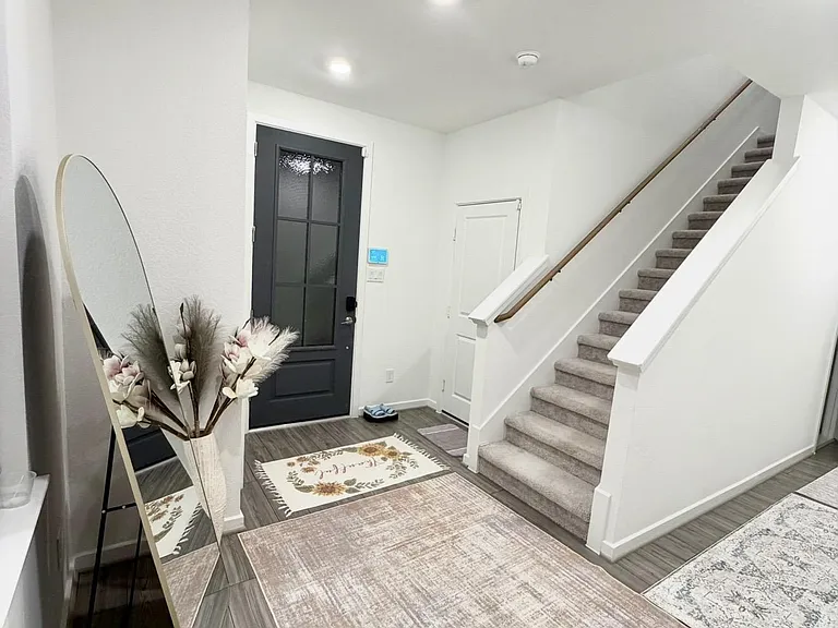 Welcoming entry foyer with durable flooring, convenient under-stair storage, and a carpeted staircase leading upstairs.
