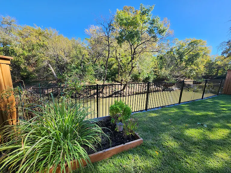 View of creek and forest; raised garden bed and baskets on fence are watered by automated sprinkler system