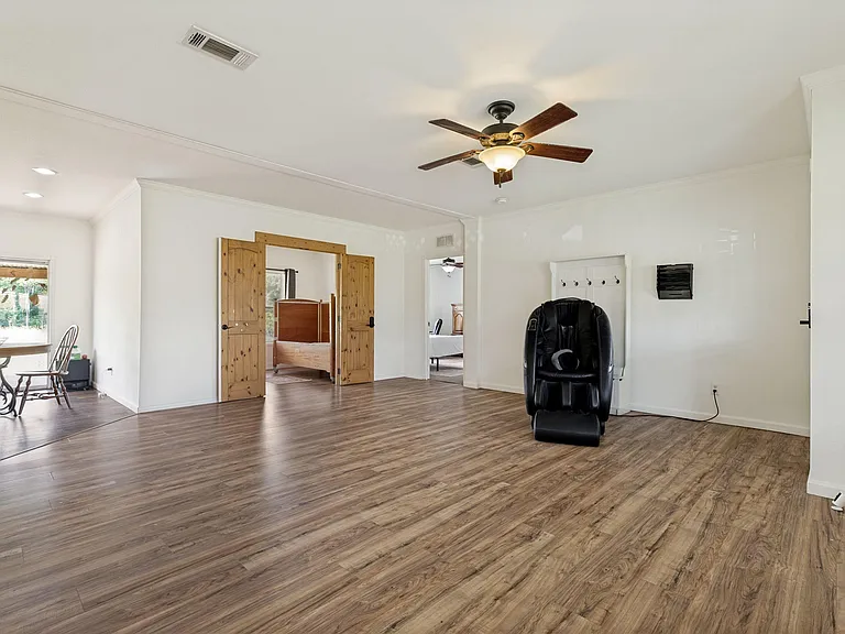 Spacious open living area with wood-look floors, ceiling fan, and wide doorway connections to adjacent rooms.