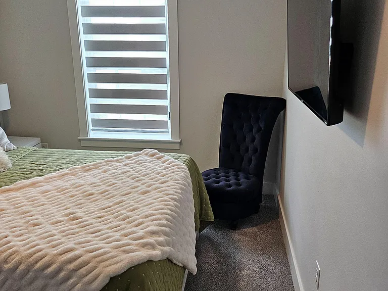 Furnished bedroom with a comfortable bed, carpeted floors, and a window with dual-layer shades for light and privacy.