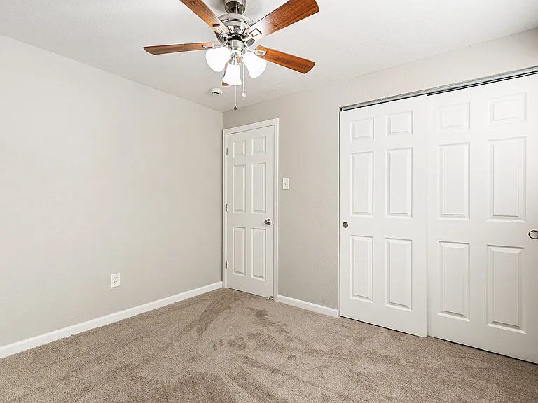 Bright and cozy carpeted bedroom with a ceiling fan and double door closet, perfect for comfort and style.