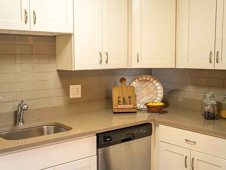 Modern kitchen with sleek countertops, stainless steel sink, and stylish cabinetry, complemented by decorative jars and a charming 'EAT' sign.