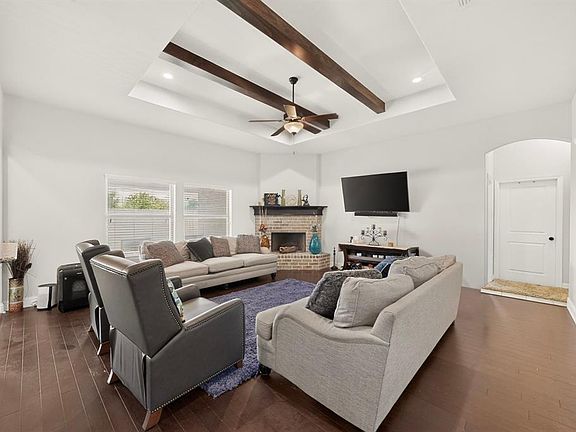 Living area featuring wood-finish flooring, a tray ceiling with exposed wood beams, and a ceiling fan