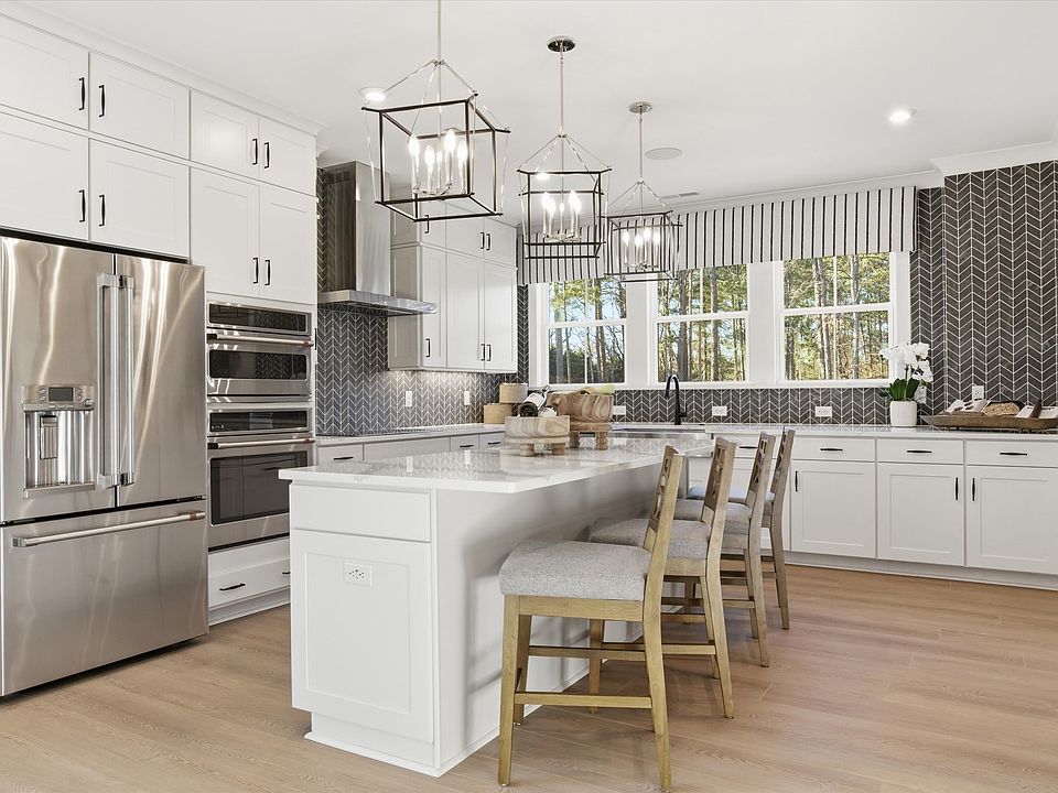 A modern, open-concept kitchen with white cabinets, a large island, and pendant lighting fixtures, s
