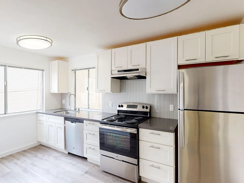 Kitchen with multiple cabinets, refrigerator, stove, range hood, and sink
