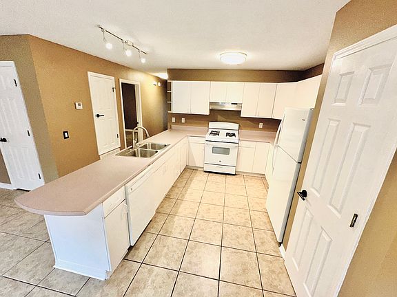Kitchen with white cabinets, matching refrigerator, and gas stove, countertops with integrated sink, and tiled flooring. Light brown walls and overhead lighting create a bright, functional space with a pantry.