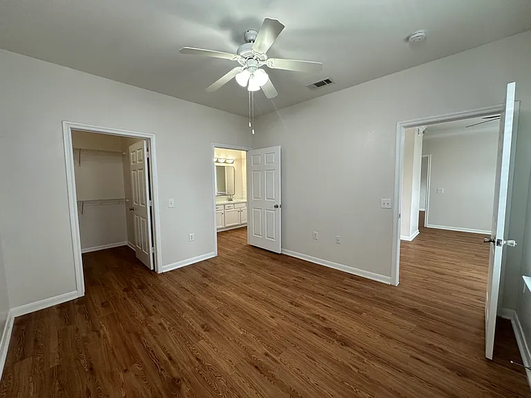 Bright and inviting bedroom with elegant wood-style flooring, a ceiling fan, and access to a walk-in closet and ensuite bathroom. Bright and inviting bedroom with elegant wood-style flooring, a ceiling fan, and access to a walk-in closet and ensuite bathr