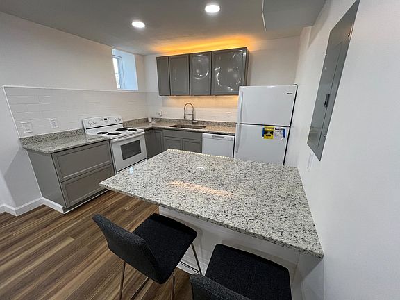 Sleek, modern kitchen with grey cabinetry, granite countertops, and white appliances. Features ample storage, a spacious island with seating, and integrated lighting for a contemporary look. Perfect for cooking and casual dining.