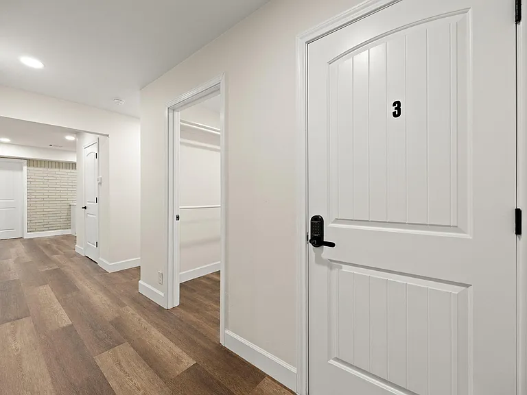Clean, well-lit hallway with durable wood-style flooring, multiple interior doors, and convenient storage/closet space.