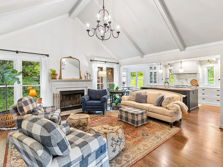 Spacious and bright living room with vaulted, beamed ceilings, a Smart TV, a fireplace, and windows looking out to the wooded backyard. Located just off the kitchen and dining area.