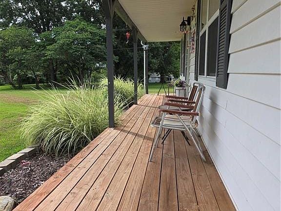 Expansive wood deck with a white vinyl siding exterior, black window shutters, and a covered porch