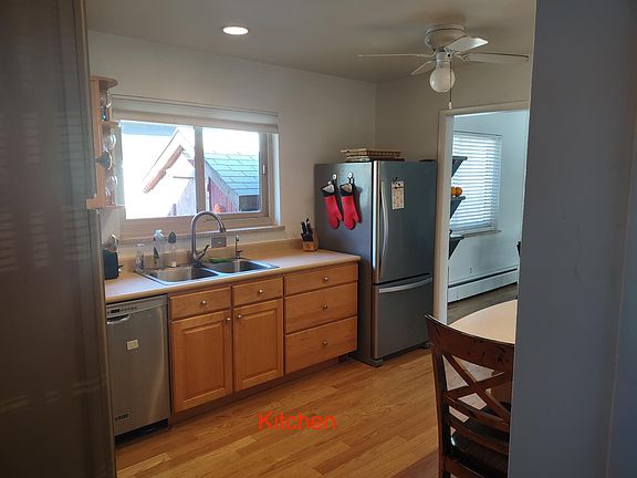 Kitchen view with fridge, dishwasher, garbage disposal, ceiling fan, and built-in table for two.
