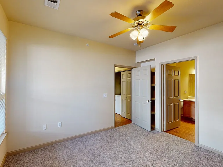 Spacious apartment bedroom with attached bathroom and plush carpet flooring.