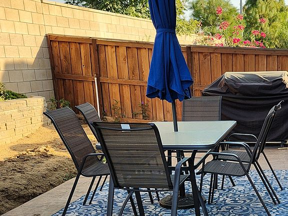 Patio table and chairs. Grill in background. There is grass on the dirt now.