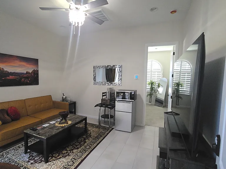 This bright lounge features a large TV on a stand with an electric fireplace below, a marble-top coffee table, and floor-to-ceiling velvet curtains. Tiled floors and modern decor create a cozy space, with color-changing fireplace lighting for added mood.