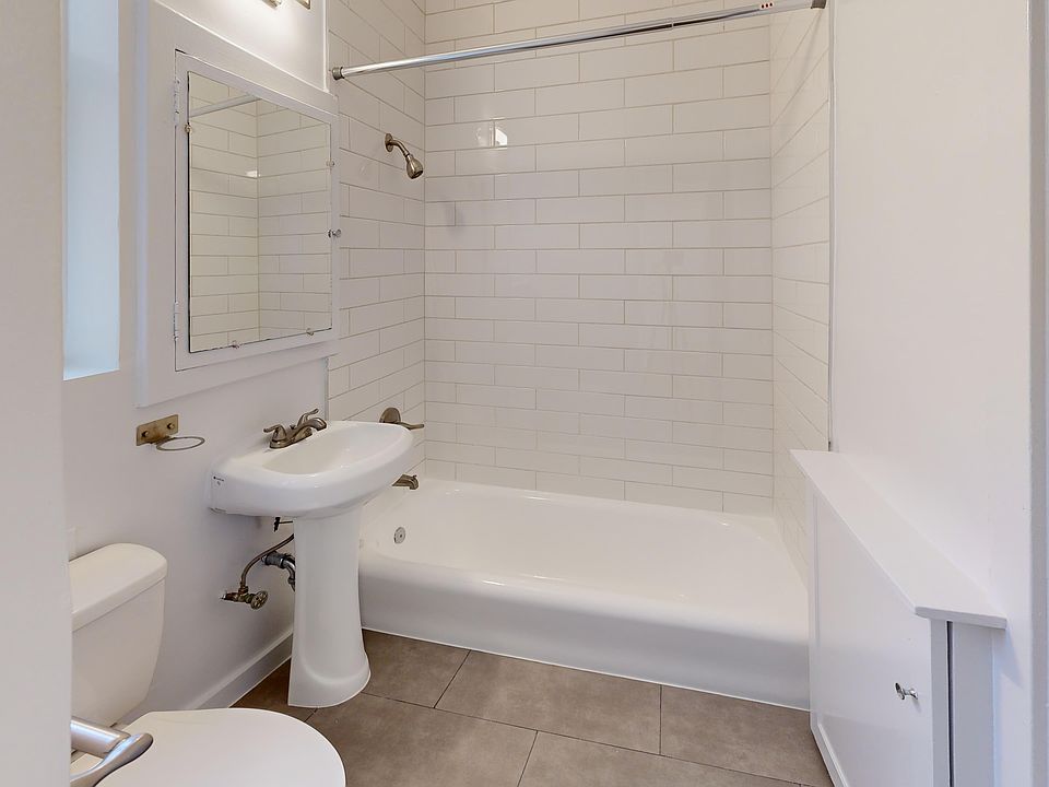 Bright, modern bathroom featuring a bathtub, pedestal sink, and tile walls with a large mirror above the sink.