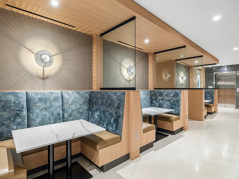 Elegant and modern lobby featuring stylish booth seating with plush blue and tan upholstery, marble-topped tables, and sophisticated wall lighting.