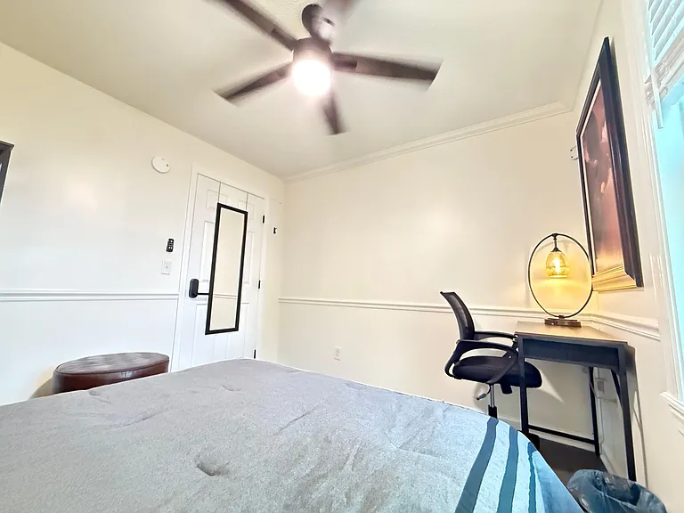 Private bedroom with ceiling fan, window blinds, and a dedicated desk/workspace plus mirror for added convenience.