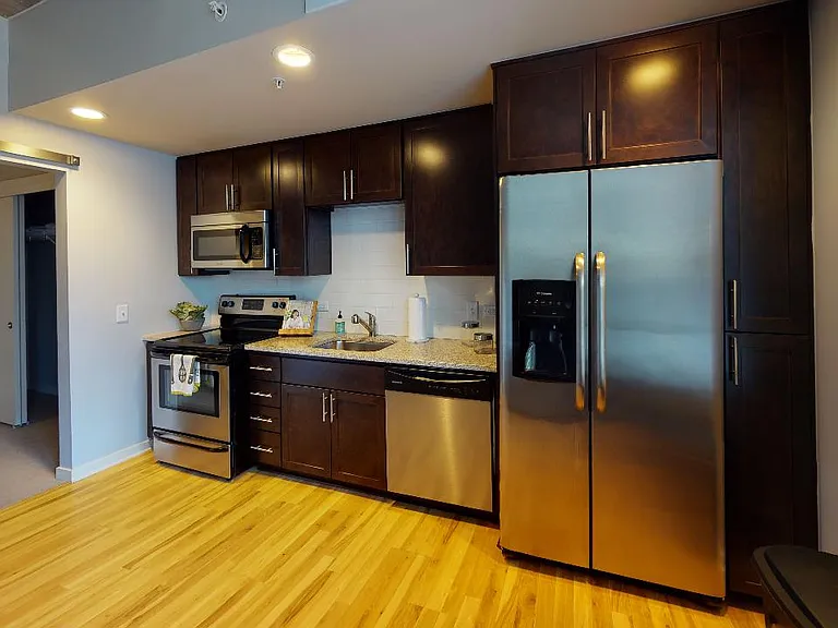 Apartment kitchen with stainless steel appliances, granite countertops and wood-style flooring.