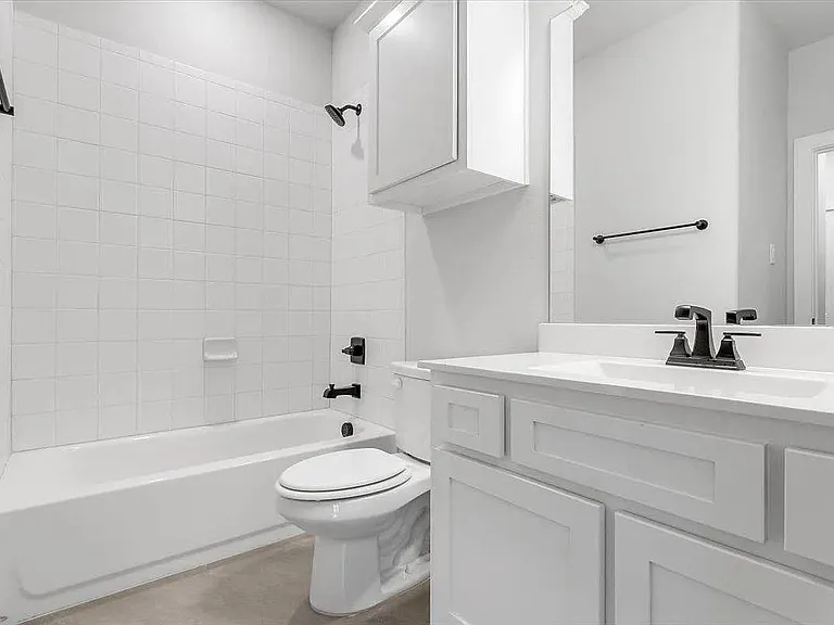 Bathroom featuring a white subway tile tub surround, white vanity with integrated sink, matte black faucet, and white shaker-style cabinetry