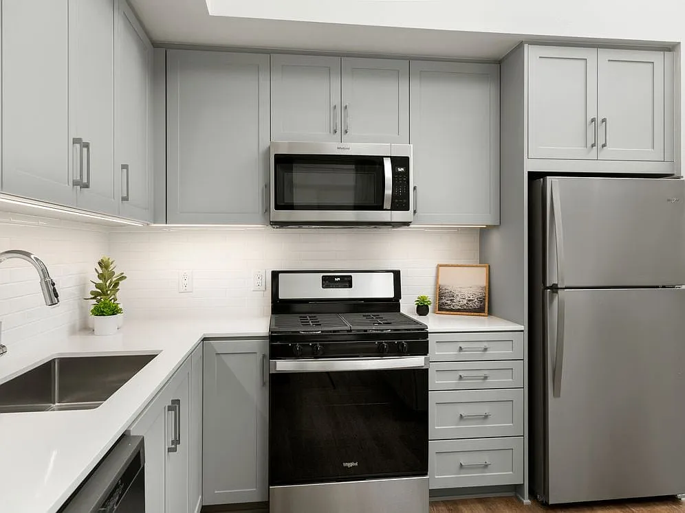 Apartments with modern kitchens featuring grey cabinetry, white quartz stone countertops, white tile backsplash, stainless steel appliances, and hard surface flooring - Avalon Monrovia