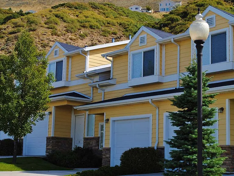 Liberty Hill Apartments, Draper, Utah, yellow townhome with a white garage door and a tree in front.