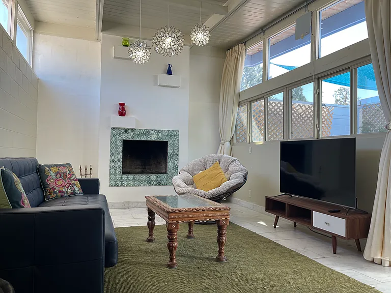 Living Room: High ceiling, stone tile floor, high windows facing east for morning light, large windows facing west, with private patio view. Functioning fireplace. Smart tv. Leather sofa that converts to a queen sized guest bed.