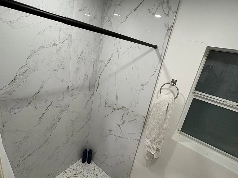 Updated walk-in shower with large-format marble-look tile, hex mosaic floor, and a window for ventilation.