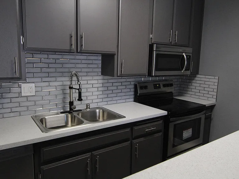 White tiled kitchen with stainless steel fridge, microwave, and oven.