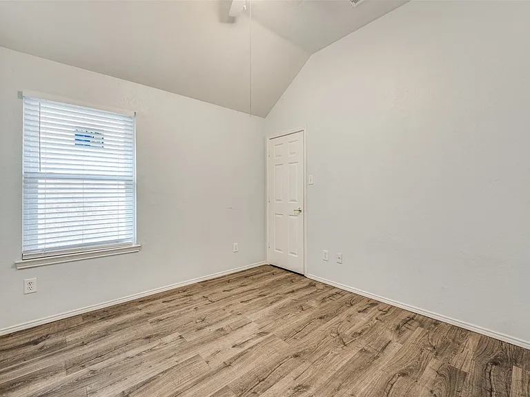 Vaulted ceiling room featuring wood-finish flooring, a white paneled door, and a single window with blinds