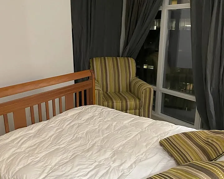 Bedroom sitting area is part of glassed wall wrapping at corner. View of balcony is seen through glass behind chair while the length of glass wall overlooks Yonge Street below