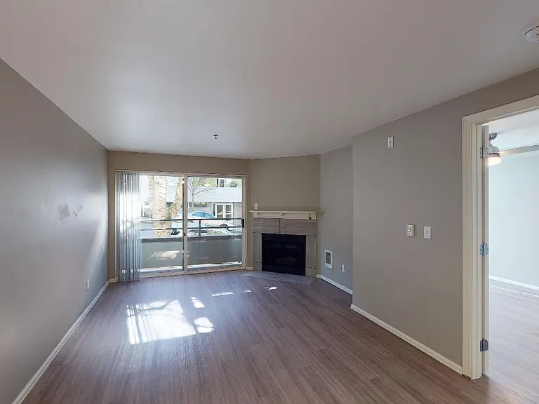 Apartment living room with wood-style flooring, balcony and fireplace in select homes.