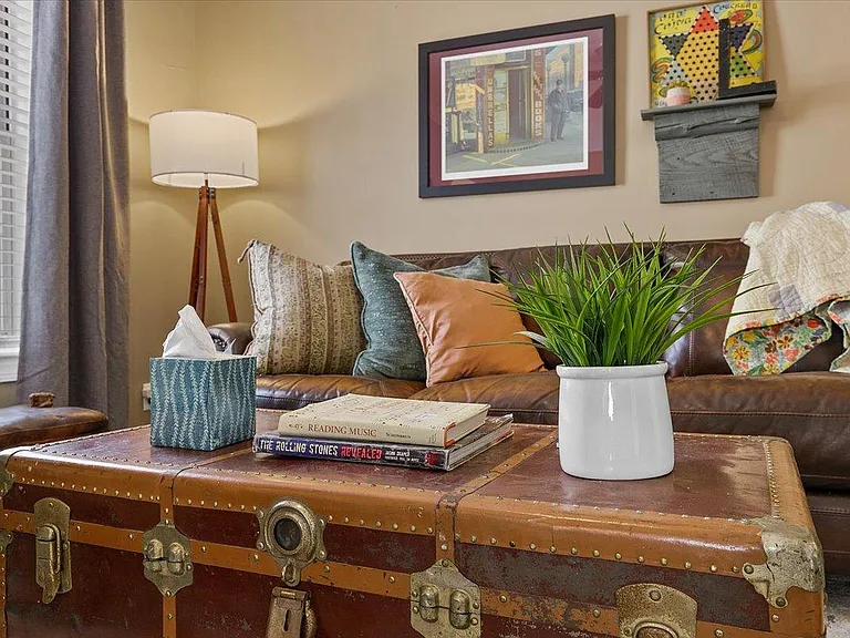 Cozy living room at Hunsucker's Place near Downtown Greensboro, featuring a comfortable leather couch, a functional writing desk, and an open-concept design connecting to the dining room with a piano and the fully equipped kitchen_perfect for relaxation