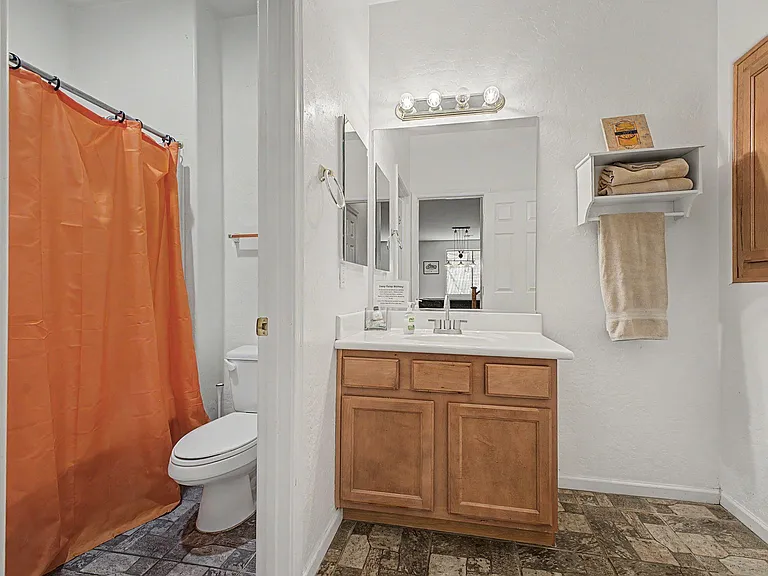 Full bath with a single-sink vanity, wall mirror, and shower/tub combo, plus open shelving for towels and essentials.