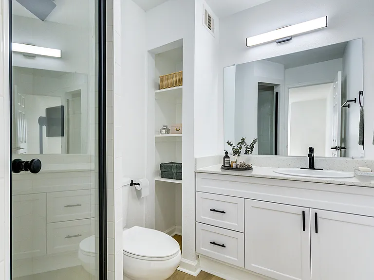 A bright, renovated bathroom with white cabinetry and black finishes is shown at ReNew on Cantrell.
