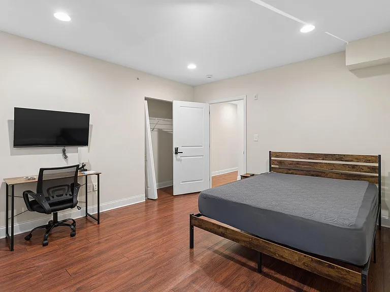 Private bedroom with hardwood floors, a roomy closet, and space for a bed plus a dedicated work desk and wall-mounted TV.
