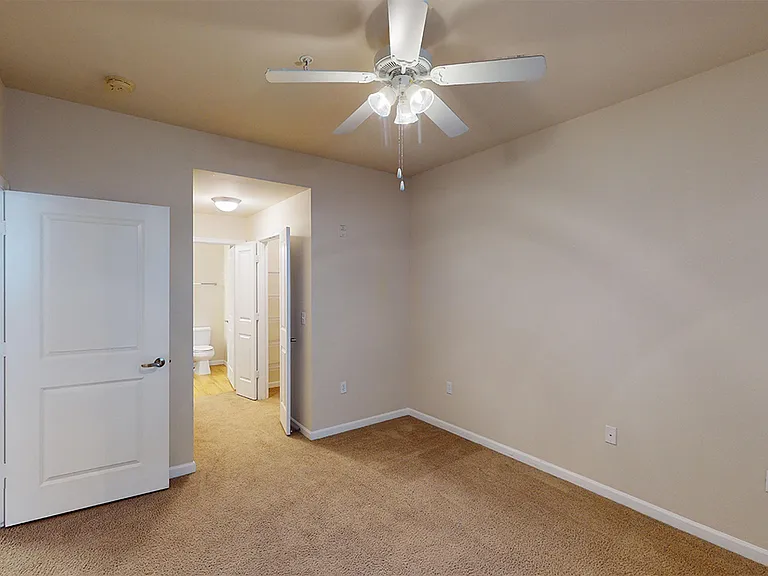 Spacious apartment bedroom with large closet, attached bathroom and plush carpet flooring.