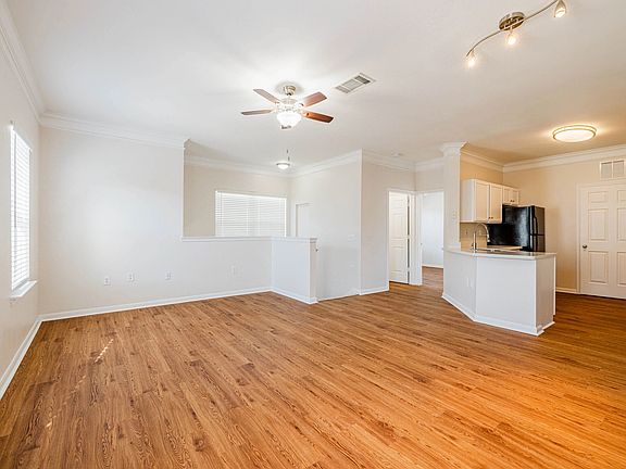 Spacious open-concept living area with wood-style floors and modern lighting, leading to a sleek kitchen with a breakfast bar. Spacious open-concept living area with wood-style floors and modern lighting, leading to a sleek kitchen with a breakfast bar.