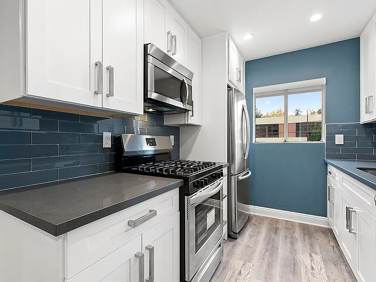 Blue tiled kitchen with stainless steel fridge, oven, and microwave.