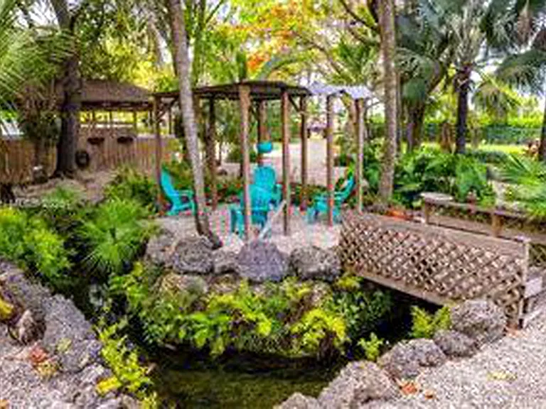 Tropical garden and pond area featuring a wooden footbridge, shaded seating area and lush mature landscaping.