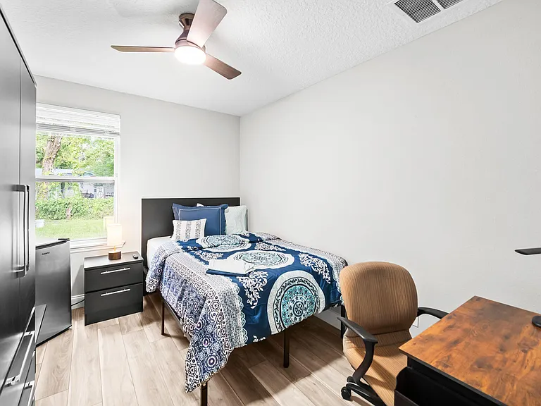 Furnished bedroom with a full bed, nightstand, wardrobe storage, and a work desk, plus a window and ceiling fan.
