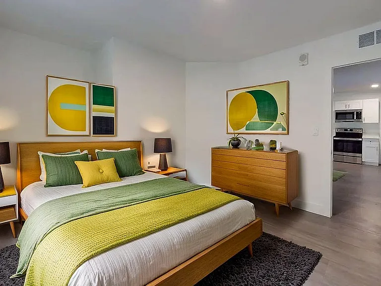 Elegant bedroom with modern wooden furniture, vibrant green and yellow decor, and a cozy ambiance. Accessible hallway leading to a sleek, contemporary kitchen.