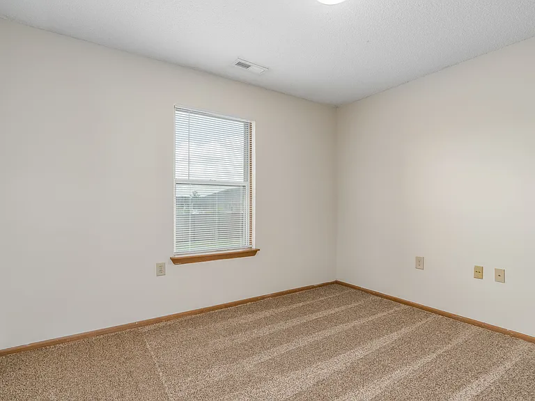 Carpeted bedroom and window with blinds of River Valley apartment home in Lancaster, OH.