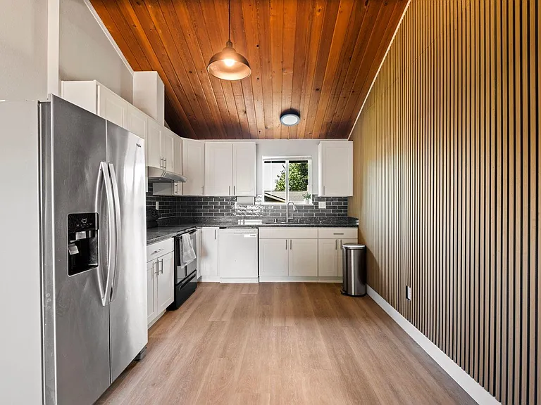 Spacious kitchen with ample white cabinetry, stainless appliances, tile backsplash, and a window over the sink.