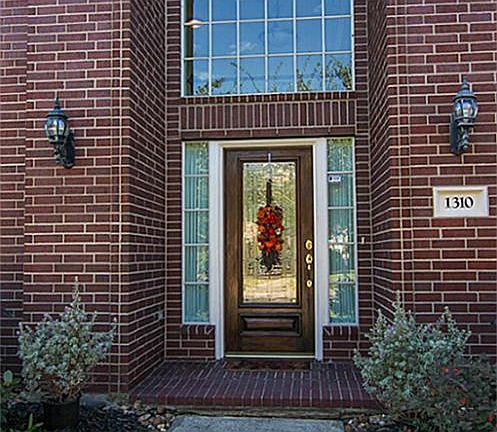 This stunning entry welcomes your guests with an arched window, wood and leaded-glass front door and brick patio.
