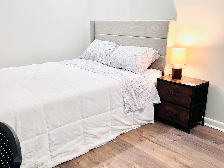 Furnished bedroom with a full bed, upholstered headboard, nightstand lighting, and durable wood-look flooring.