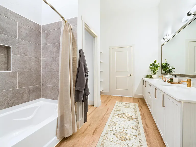Primary bathroom with a tiled soaking tub, extended vanity, and warm wood style flooring designed for everyday comfort and easy routines.